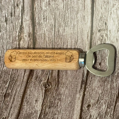 Vue de dessus du décapsuleur en bois clair gravé avec la phrase humoristique sur l'eau et l'alcool.