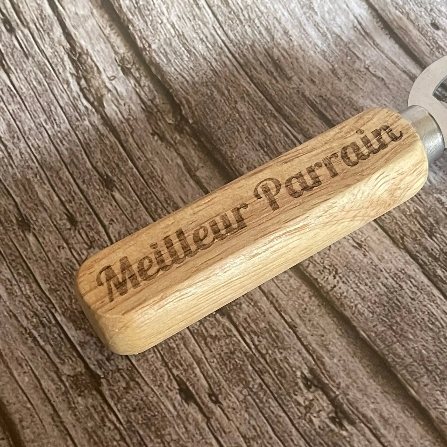 Gros plan sur la qualité de la gravure profonde "Meilleur Parrain" sur le manche en bois.